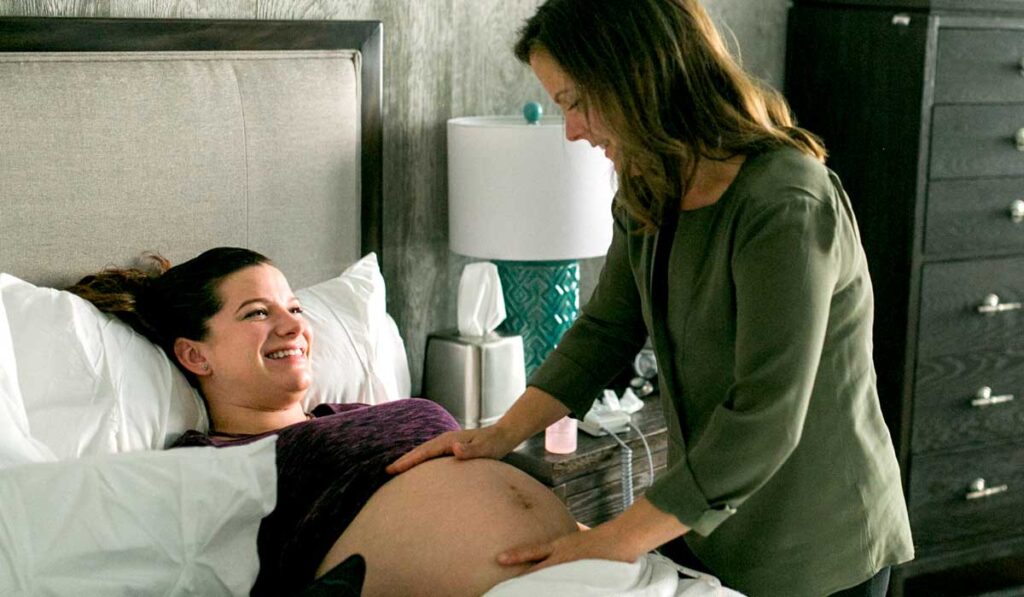 Pregnant woman laying down with another rubbing pregnant belly