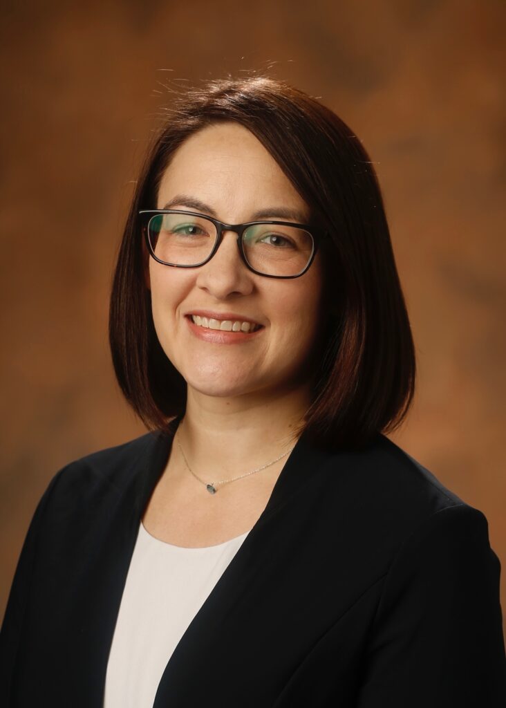 Sharon Davis, Ph.D., portrait. Dark hair, glasses, black jacket, white shirt