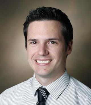 Portrait of Dr. Ryan Stark, a white man in a white coat with a necktie. Brown hair.