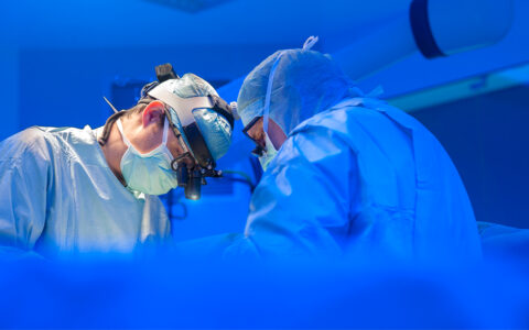 Surgeons in surgical suite with patient obscured. Blue overtones
