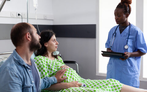 African American nurse speaking with a pregnant woman and her partner in hospital ward.