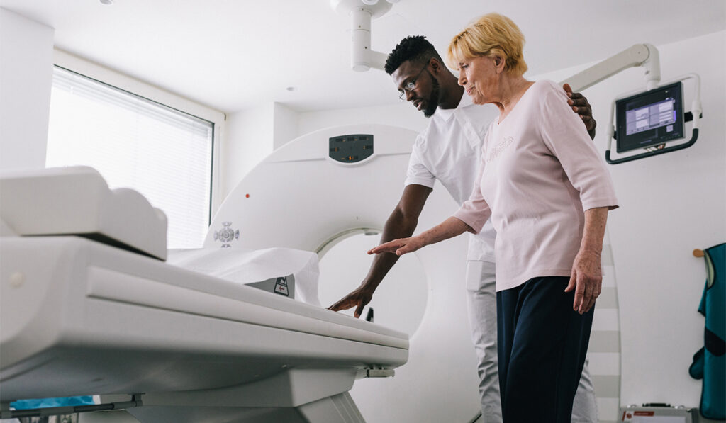 Male staff guides an elderly woman to an MRI machine