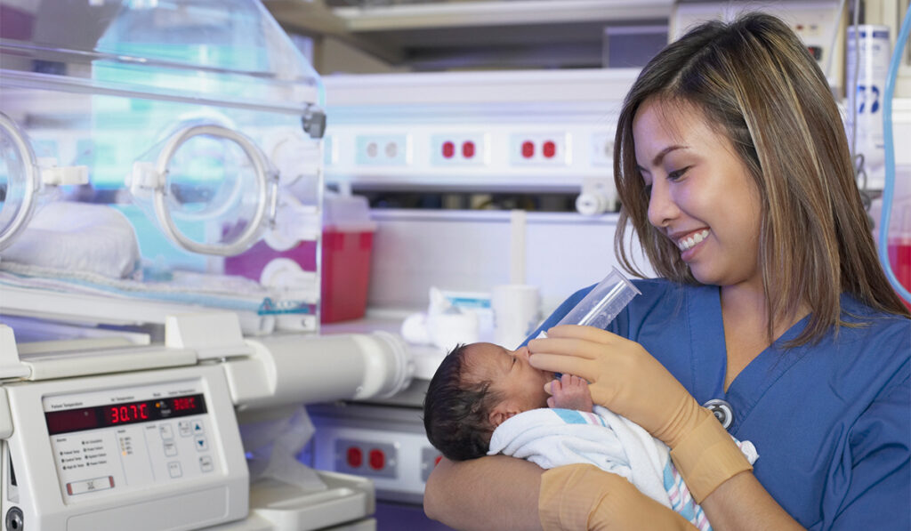 Female nurse feeding newborn Black baby next to an incubator