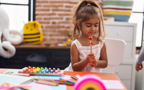 Young Hispanic girl playing xylophone sitting on table at kindergarten