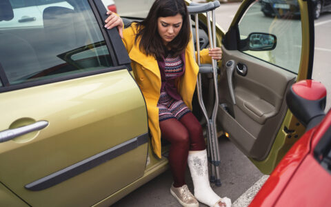 Woman with crutches getting out of the passenger side of a car