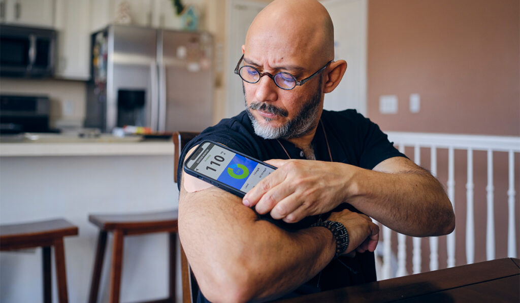 mature man in a home checking his blood sugar with continuous glucose monitor