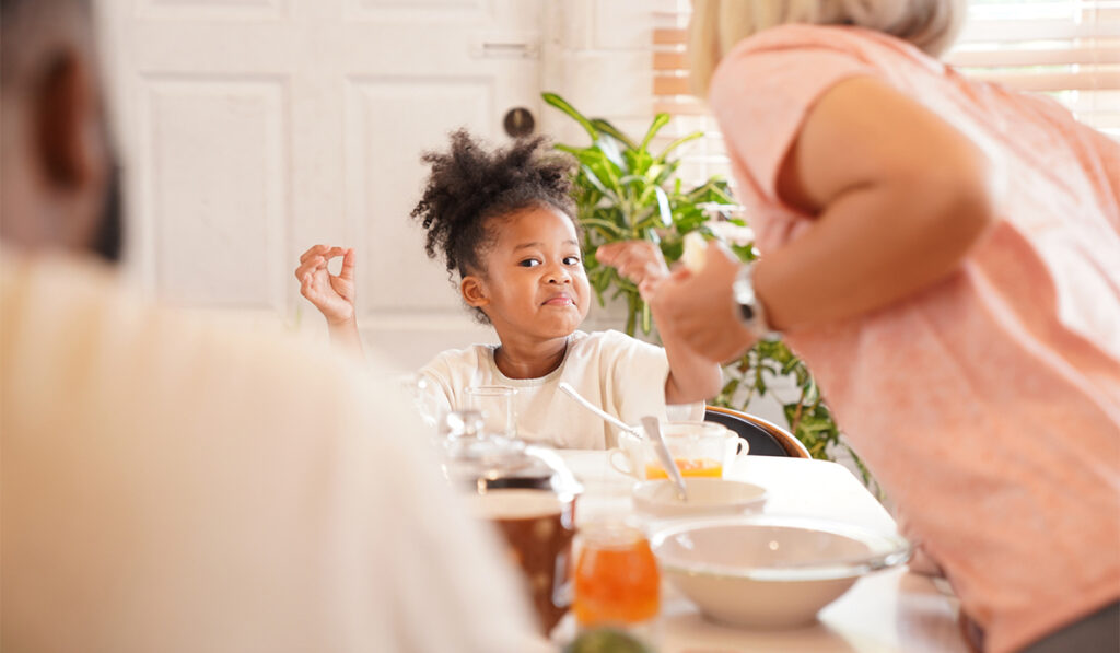 Girl at dining table makes a playful expression to father