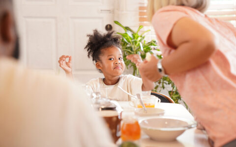 Girl at dining table makes a playful expression to father