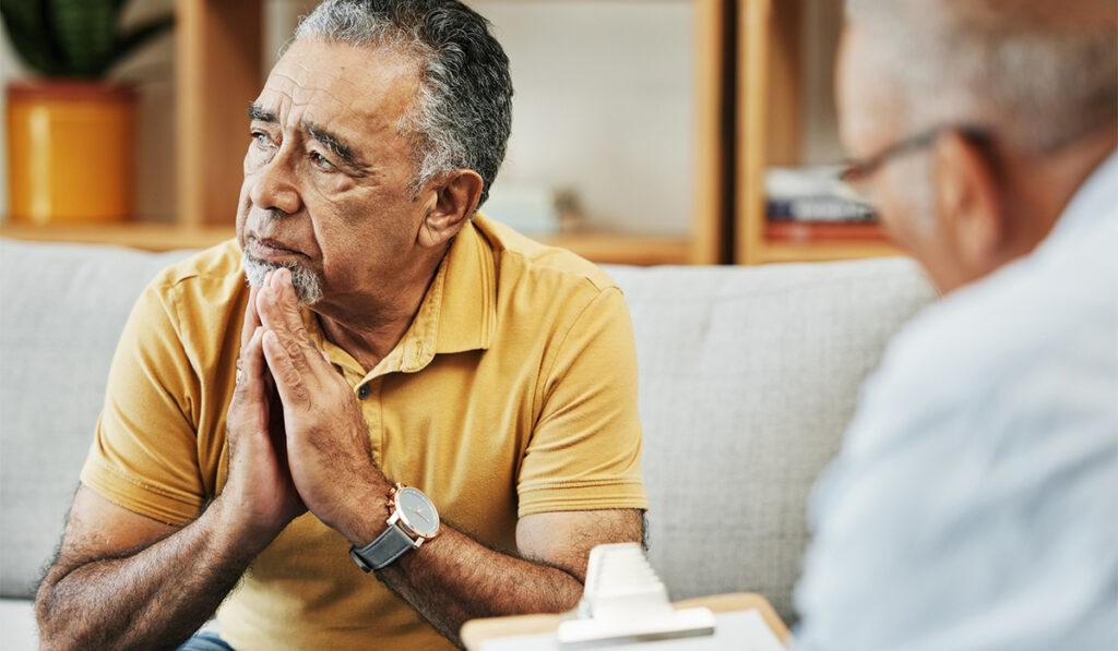 Mature hispanic man sits on a couch talking with a therapist or psychologist