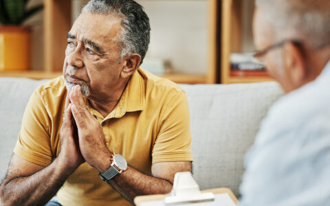 Mature hispanic man sits on a couch talking with a therapist or psychologist